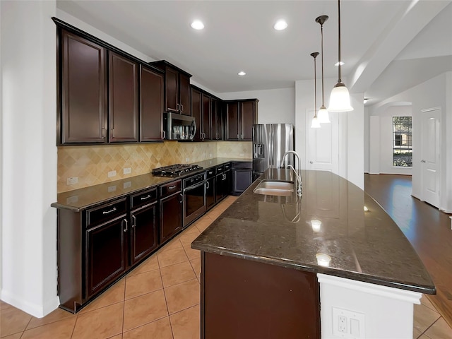 kitchen with tasteful backsplash, stainless steel appliances, sink, pendant lighting, and an island with sink