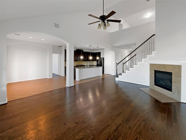 unfurnished living room featuring high vaulted ceiling, ceiling fan, dark hardwood / wood-style floors, and a tile fireplace