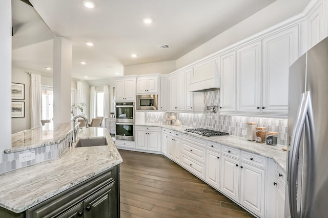 kitchen featuring custom range hood, stainless steel appliances, a kitchen island with sink, sink, and white cabinets