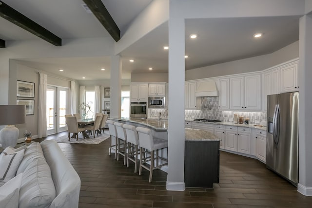 kitchen featuring beam ceiling, stainless steel appliances, light stone counters, premium range hood, and white cabinets