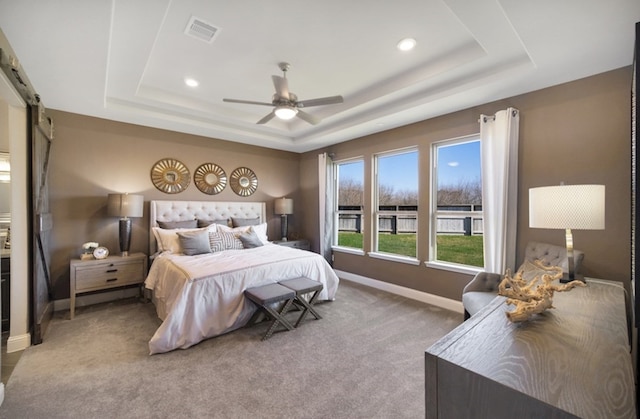 bedroom featuring a raised ceiling, a barn door, ceiling fan, and carpet