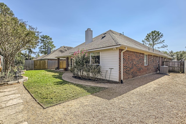 back of house with a fenced backyard, a chimney, a yard, central air condition unit, and brick siding