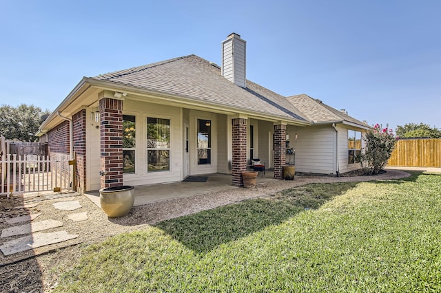 rear view of house featuring roof with shingles, brick siding, a lawn, a patio area, and fence