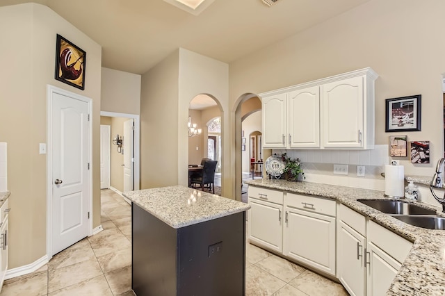 kitchen featuring arched walkways, a sink, white cabinetry, a center island, and decorative backsplash