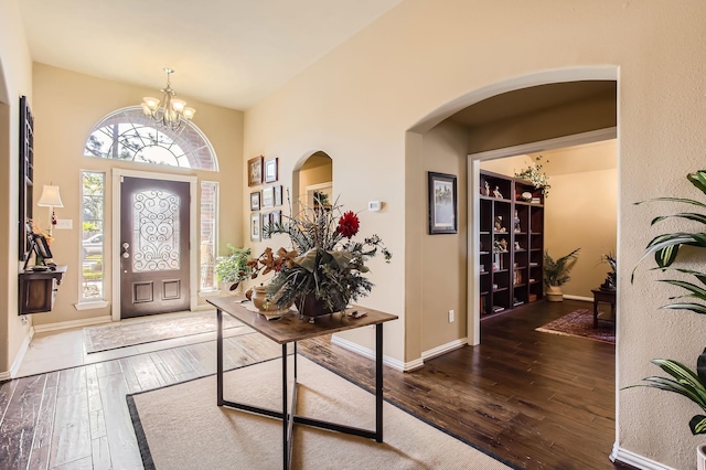 foyer entrance with a chandelier, arched walkways, baseboards, and hardwood / wood-style floors