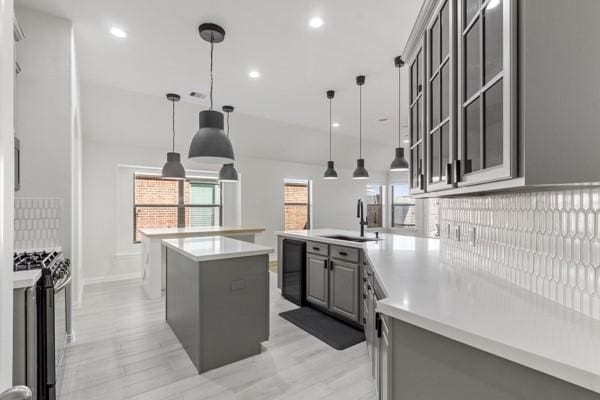 kitchen with pendant lighting, a center island with sink, sink, stainless steel stove, and gray cabinets