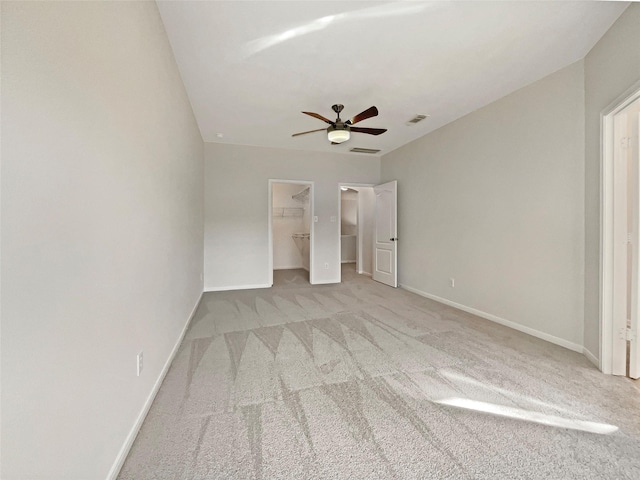 unfurnished bedroom featuring a walk in closet, ceiling fan, a closet, and light carpet