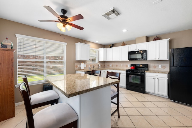 kitchen with light stone countertops, backsplash, a kitchen bar, white cabinets, and black appliances