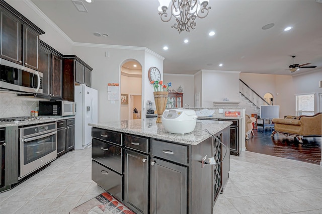 kitchen with light tile patterned floors, ceiling fan with notable chandelier, a kitchen island, pendant lighting, and appliances with stainless steel finishes