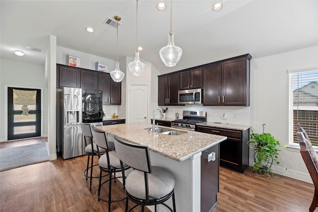 kitchen with decorative backsplash, appliances with stainless steel finishes, dark brown cabinetry, pendant lighting, and a center island with sink