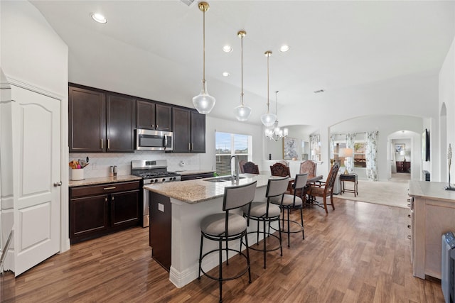 kitchen with light stone countertops, sink, hanging light fixtures, stainless steel appliances, and an island with sink