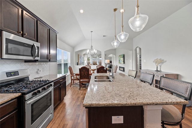 kitchen with stainless steel appliances, vaulted ceiling, sink, decorative light fixtures, and an island with sink