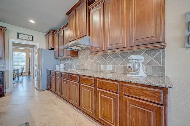 kitchen featuring appliances with stainless steel finishes, backsplash, light stone counters, and light tile patterned flooring