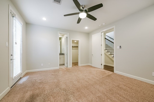 unfurnished bedroom with ceiling fan, ensuite bathroom, a walk in closet, light carpet, and a closet