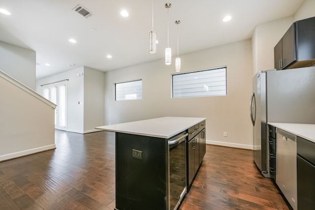 kitchen with appliances with stainless steel finishes, beverage cooler, dark hardwood / wood-style floors, a kitchen island, and hanging light fixtures