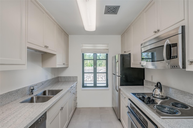 kitchen with light stone countertops, appliances with stainless steel finishes, white cabinetry, and sink