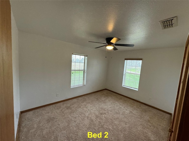 spare room with carpet floors, baseboards, visible vents, and a textured ceiling