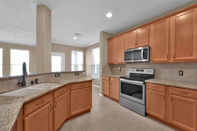 kitchen with appliances with stainless steel finishes, light stone counters, ornamental molding, sink, and light tile patterned floors