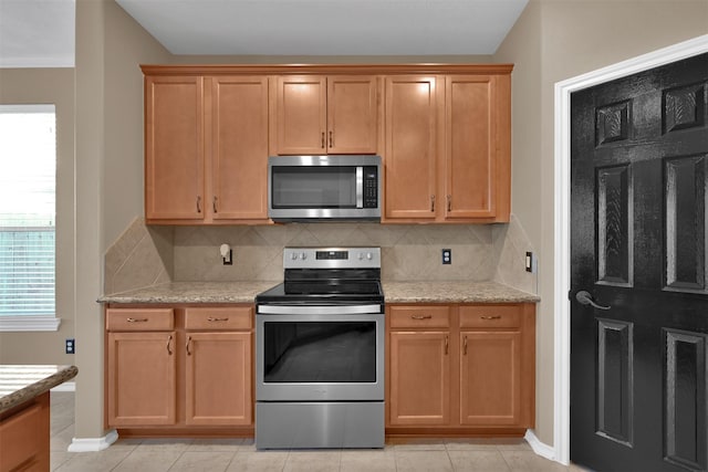 kitchen featuring decorative backsplash, appliances with stainless steel finishes, light tile patterned floors, and light stone countertops