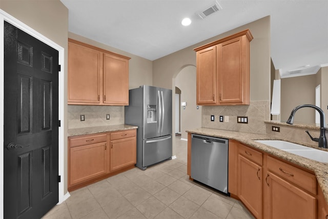 kitchen with backsplash, sink, light tile patterned floors, appliances with stainless steel finishes, and light stone counters