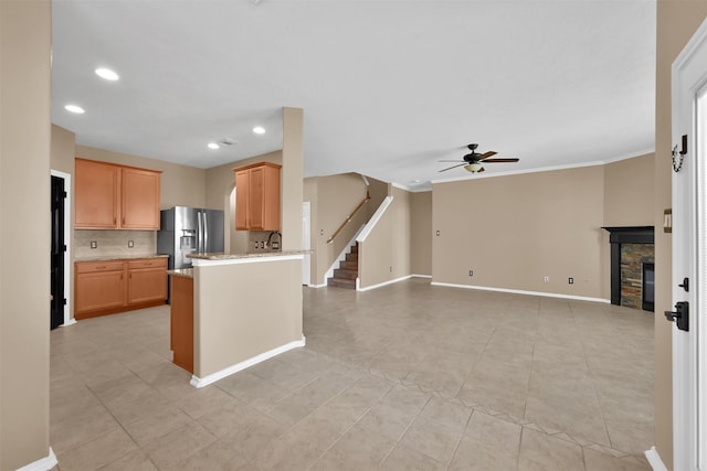 kitchen featuring sink, stainless steel refrigerator with ice dispenser, ceiling fan, a fireplace, and kitchen peninsula