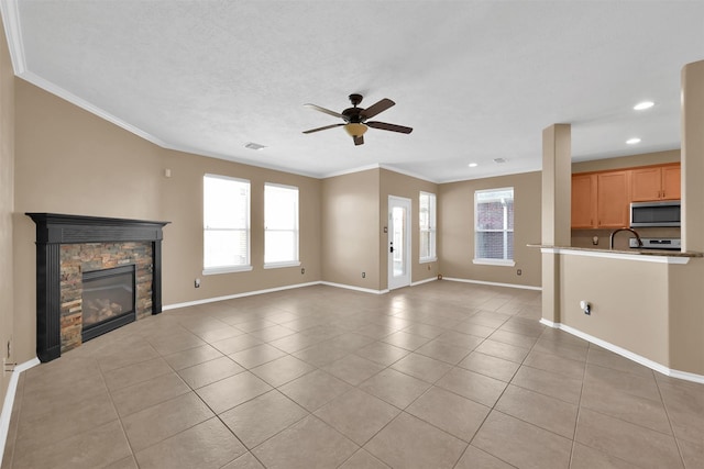 unfurnished living room with ceiling fan, sink, crown molding, a fireplace, and light tile patterned floors