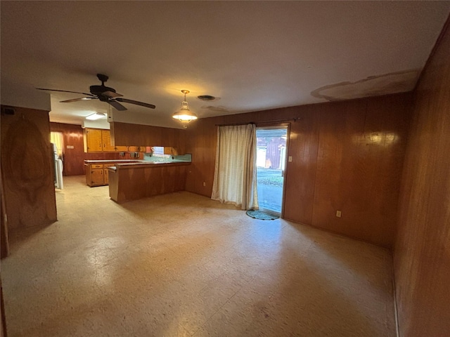 unfurnished living room featuring ceiling fan and wooden walls