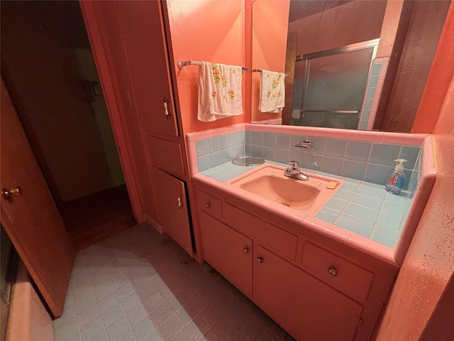 bathroom featuring vanity, a shower with shower door, and tasteful backsplash