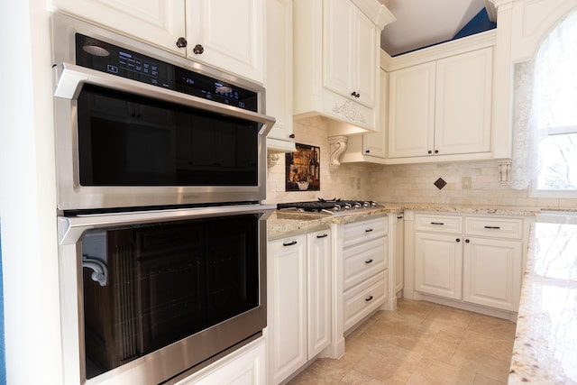 kitchen with white cabinets, appliances with stainless steel finishes, backsplash, and light stone countertops