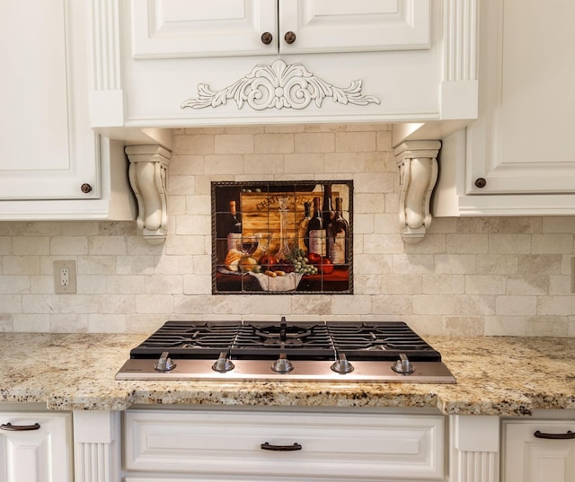 interior details with tasteful backsplash, light stone countertops, white cabinets, and stainless steel gas cooktop