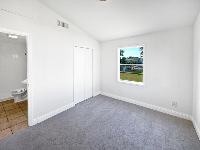 unfurnished bedroom with a closet, carpet floors, connected bathroom, and vaulted ceiling