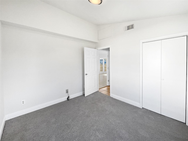 unfurnished bedroom with a closet, lofted ceiling, and dark colored carpet