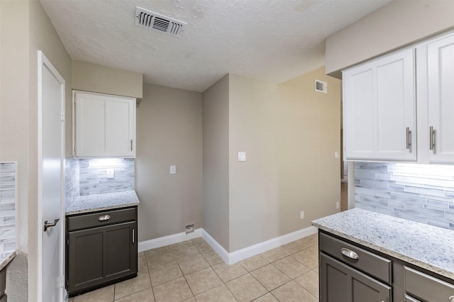 kitchen with light tile patterned floors, backsplash, white cabinetry, and light stone counters