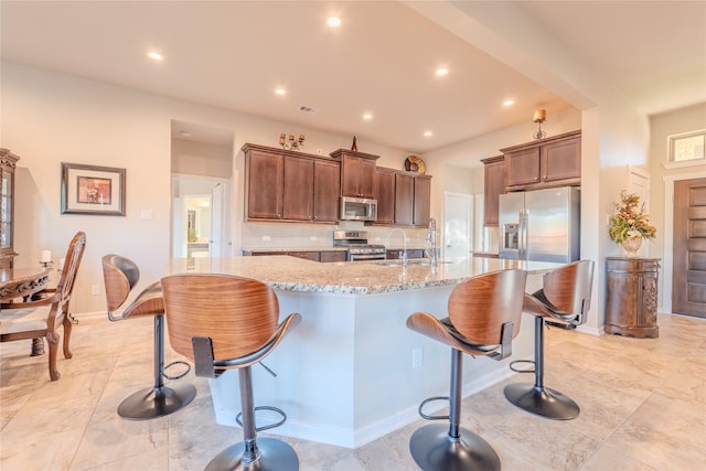 kitchen featuring light stone countertops, sink, stainless steel appliances, a breakfast bar, and a center island with sink