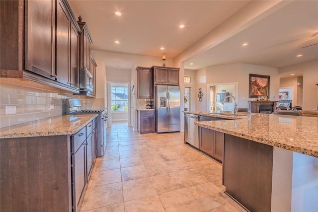 kitchen with dark brown cabinetry, light stone countertops, sink, and appliances with stainless steel finishes