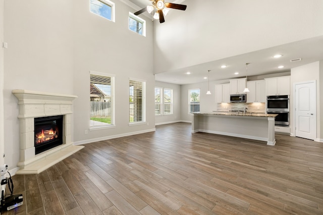 unfurnished living room with ceiling fan, a towering ceiling, and dark wood-type flooring