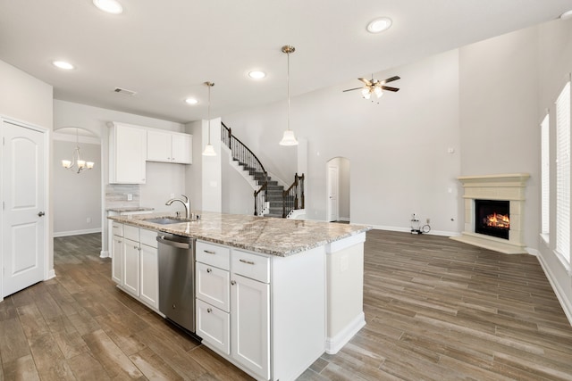 kitchen with white cabinetry, sink, light stone countertops, stainless steel dishwasher, and a kitchen island with sink