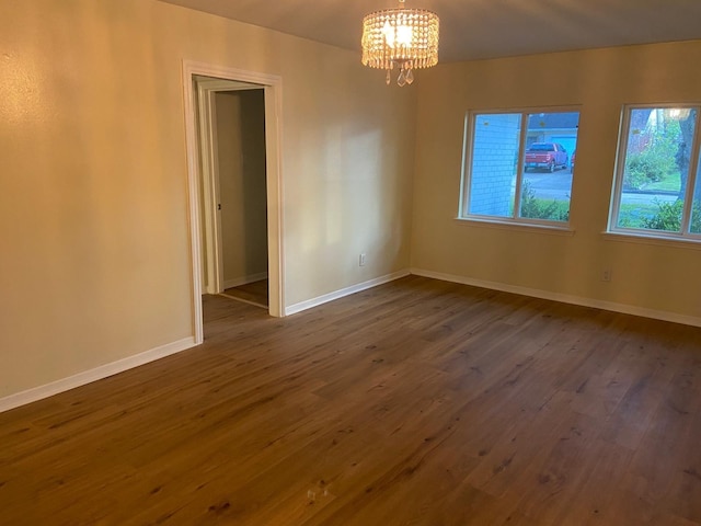 spare room with dark hardwood / wood-style floors and an inviting chandelier