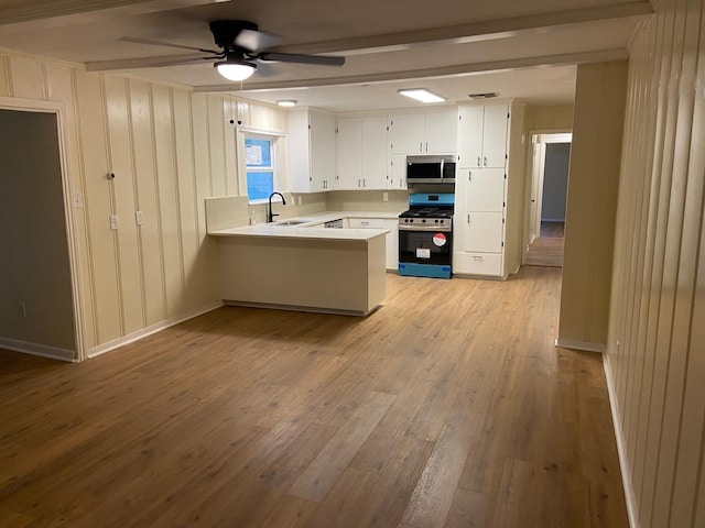 kitchen featuring kitchen peninsula, sink, ceiling fan, white cabinetry, and range with gas cooktop