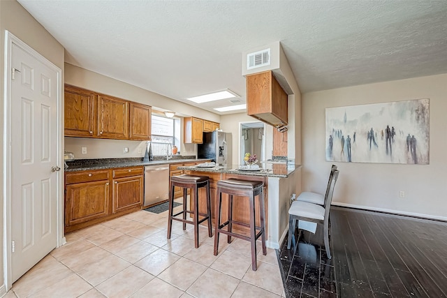 kitchen with stainless steel appliances, a kitchen breakfast bar, dark stone counters, a textured ceiling, and light tile patterned flooring