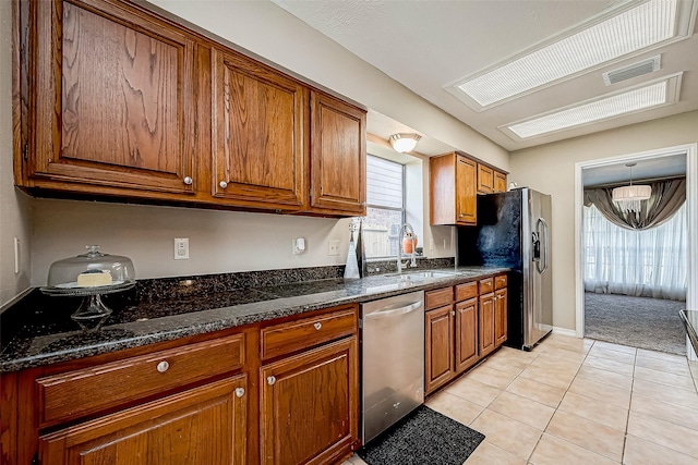 kitchen featuring light tile patterned flooring, appliances with stainless steel finishes, dark stone counters, and sink