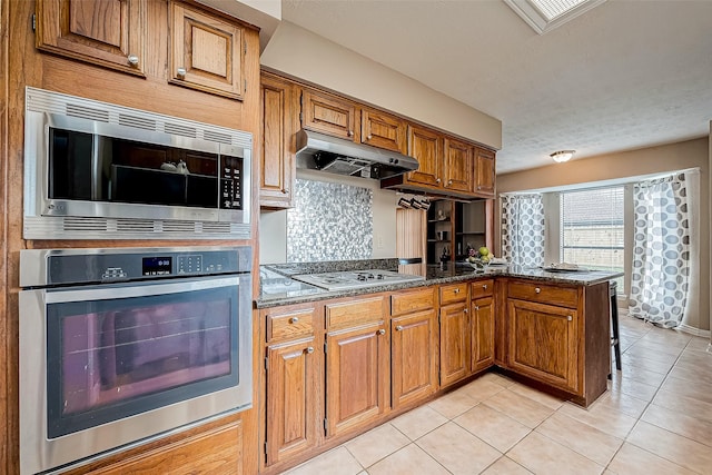 kitchen with backsplash, kitchen peninsula, light tile patterned floors, and stainless steel appliances