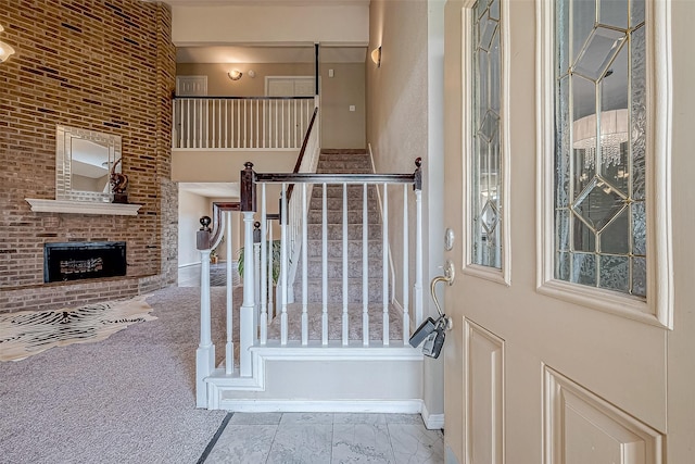 entryway with light carpet, a towering ceiling, and a brick fireplace