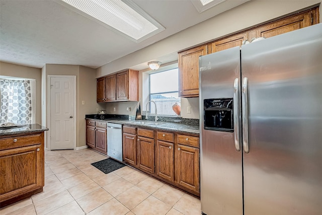 kitchen featuring a skylight, sink, dark stone counters, light tile patterned floors, and appliances with stainless steel finishes