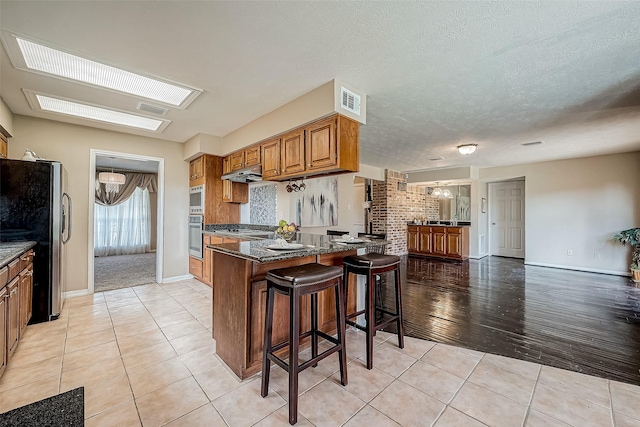 kitchen featuring kitchen peninsula, light tile patterned floors, stainless steel appliances, and a breakfast bar area