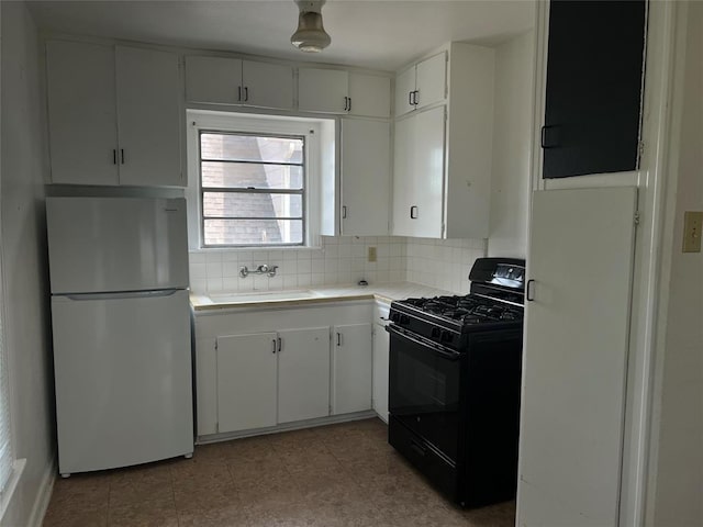 kitchen featuring sink, black gas range oven, white refrigerator, decorative backsplash, and white cabinets