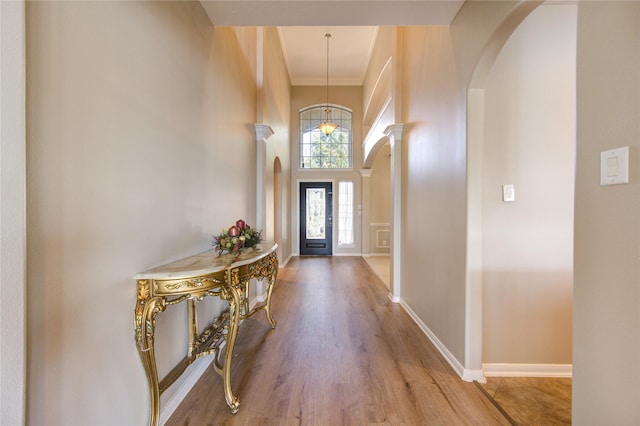 foyer entrance featuring wood-type flooring, a towering ceiling, an inviting chandelier, and ornamental molding