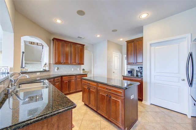 kitchen with a center island, sink, tasteful backsplash, dark stone countertops, and light tile patterned flooring