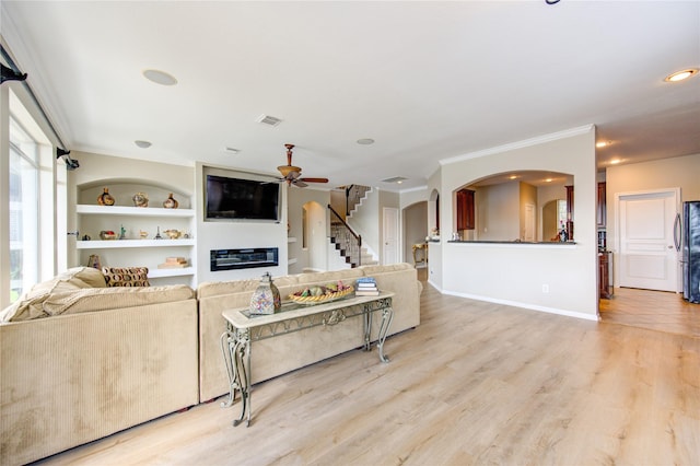 living room with crown molding, built in features, ceiling fan, and light hardwood / wood-style floors