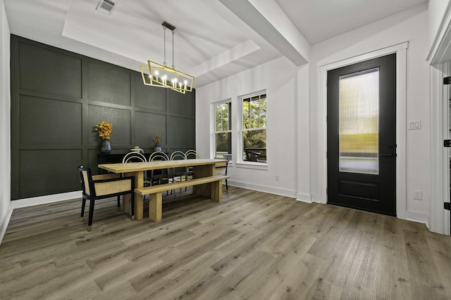 dining area with a raised ceiling, hardwood / wood-style floors, and a notable chandelier